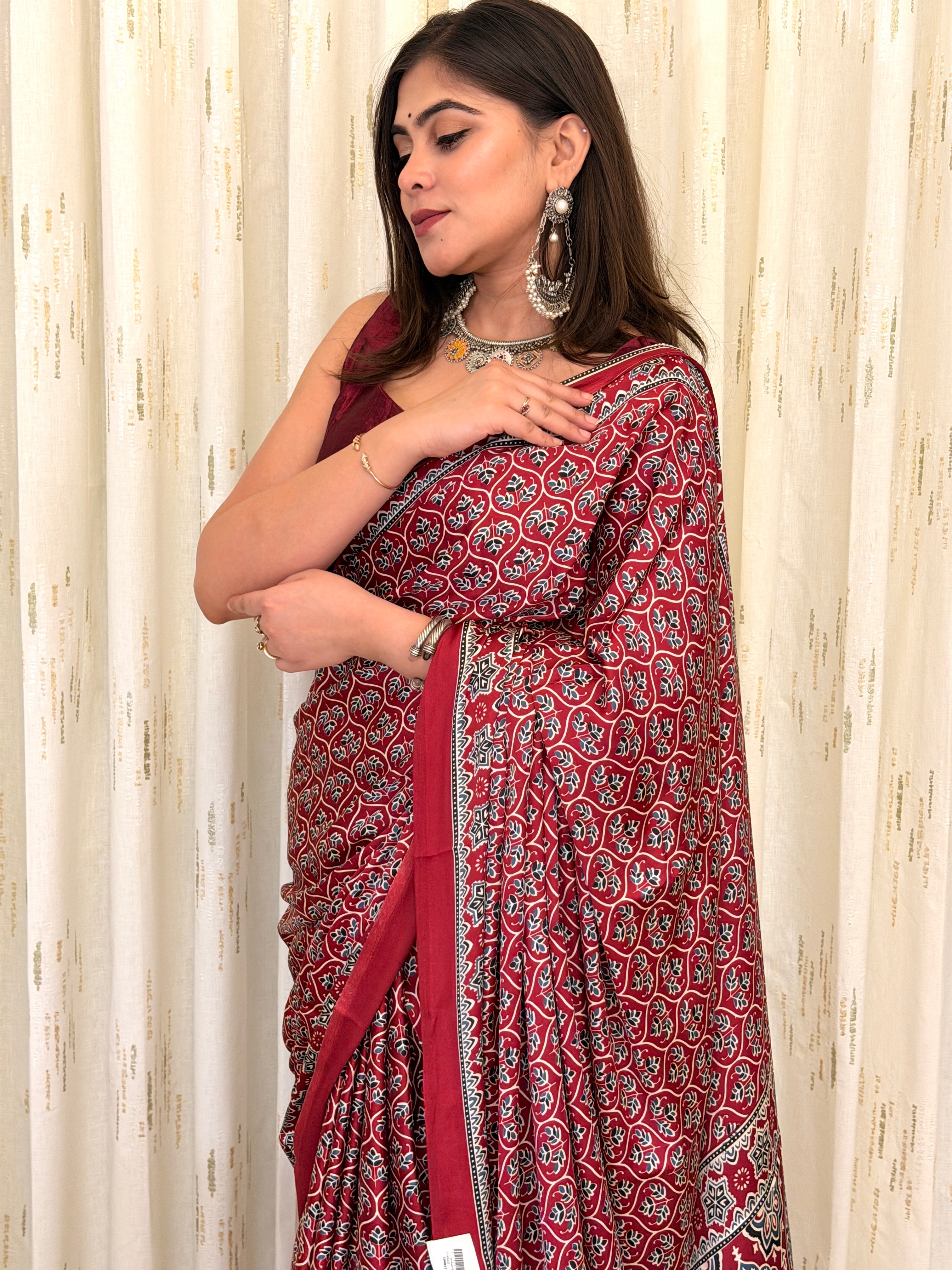 Woman in maroon Ajrakh saree adjusting pallu with silver jewellery - side pose