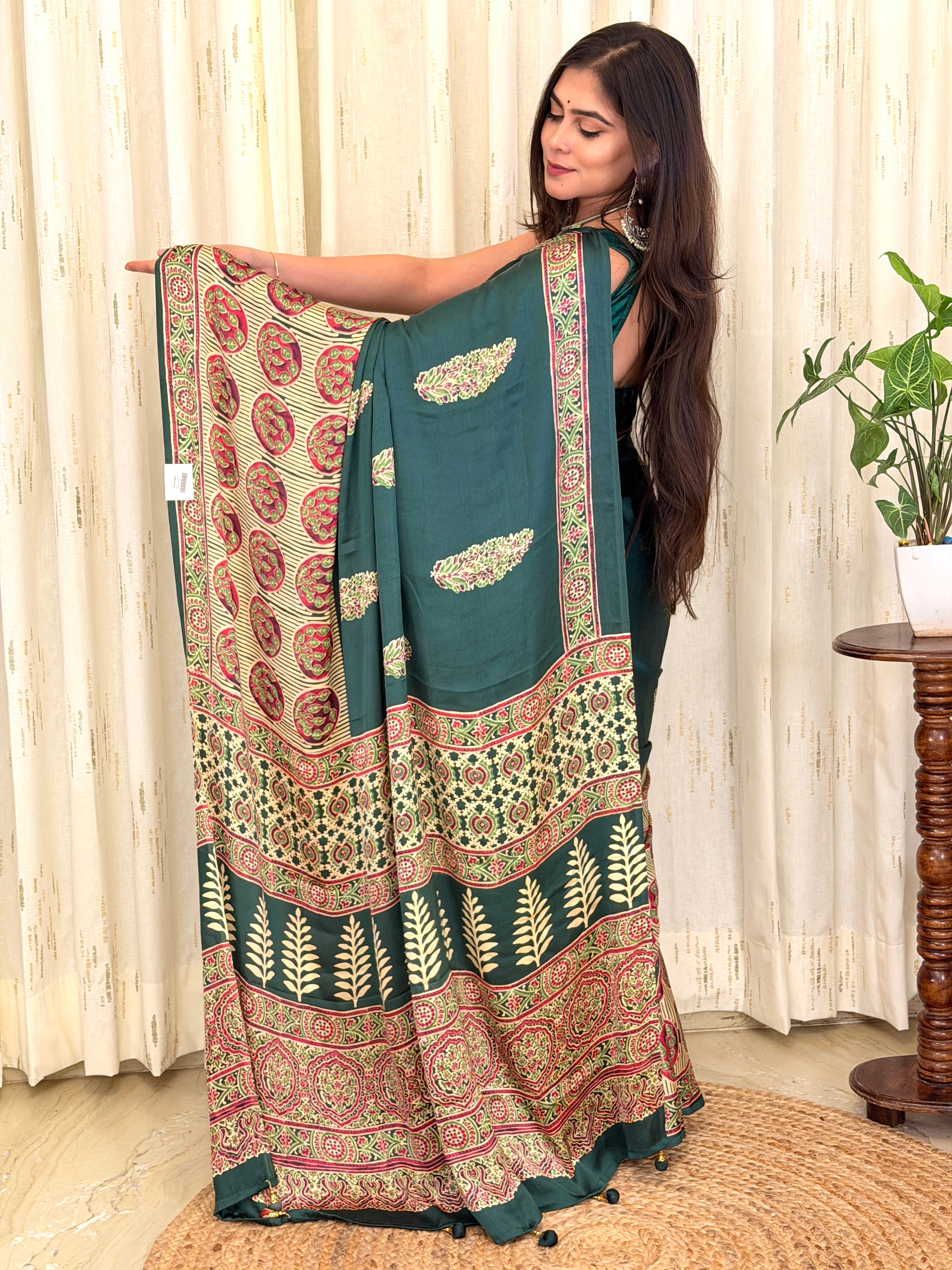 Bottle green Ajrakh leaf print modal silk saree pallu held open by model