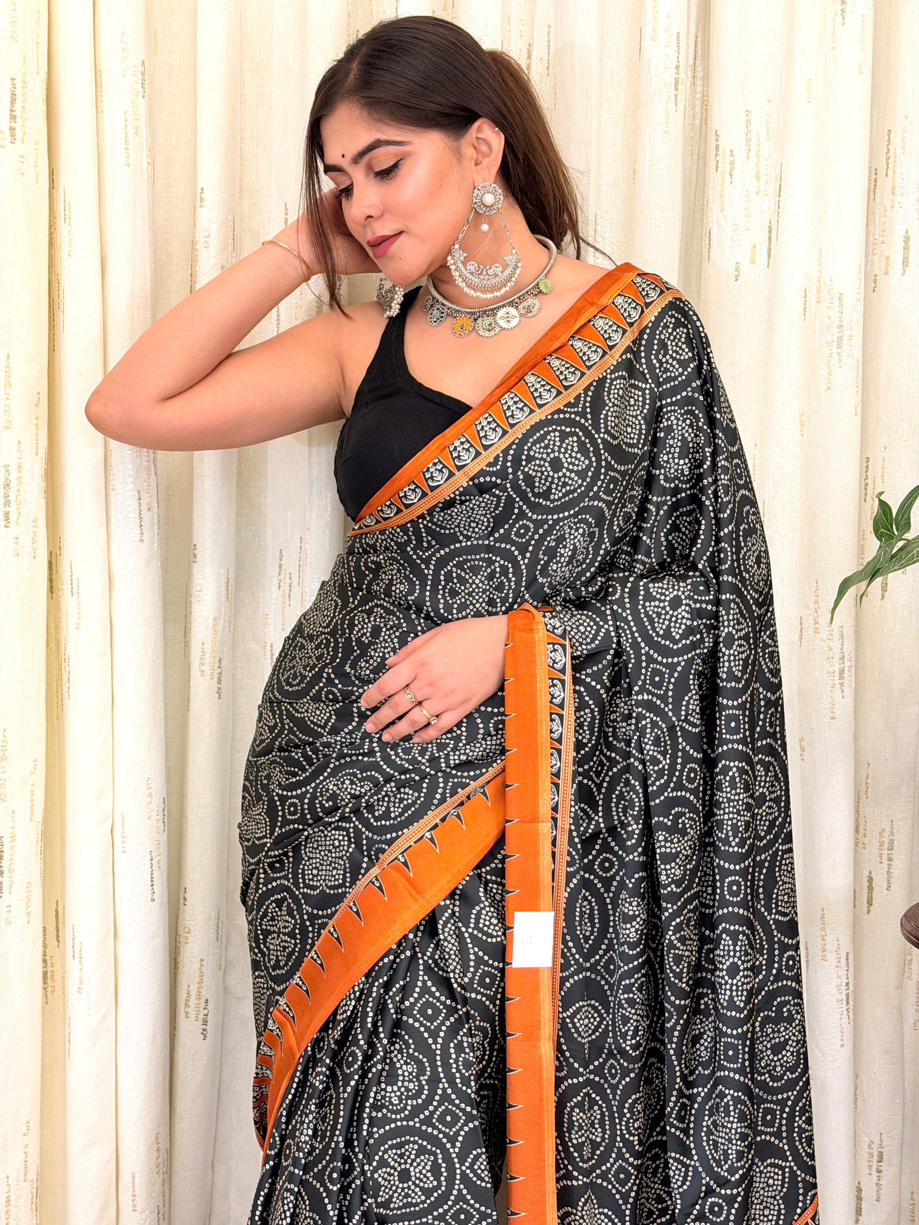 Woman draped in black and rust bandhani saree with silver jewellery - side pose