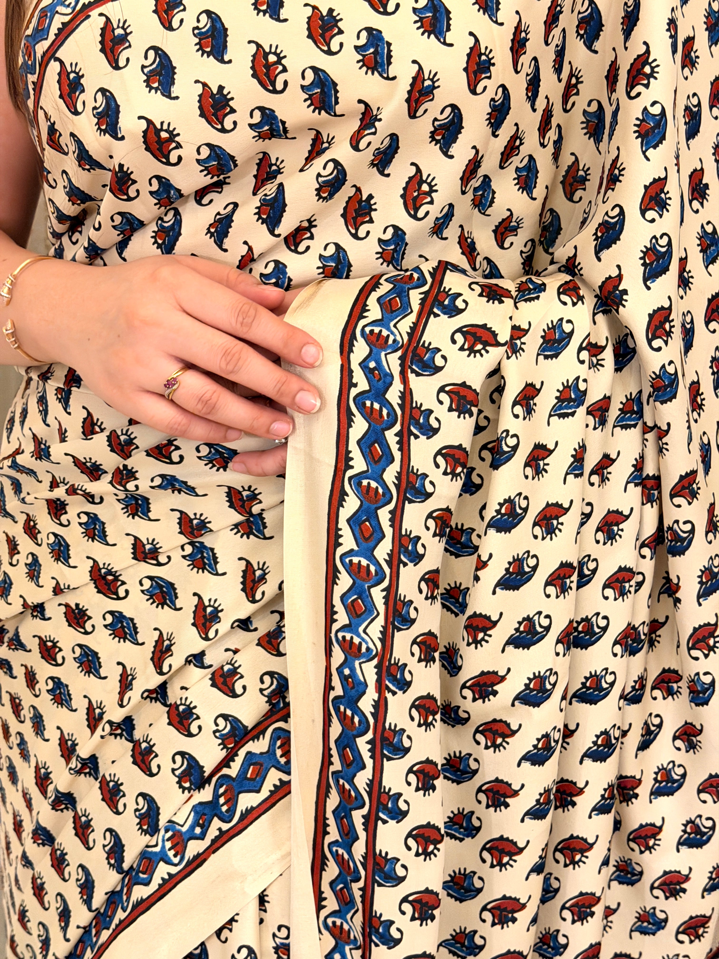 Close-up of ivory paisley print saree fabric with blue and rust border detail