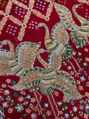 Close-up of a rich red bridal dupatta showcasing heavy gold zari and white pearl hand-embroidery. The intricate design features traditional motifs including majestic cranes, a decorated elephant, and floral vines over a textured red background with subtle dot patterns.