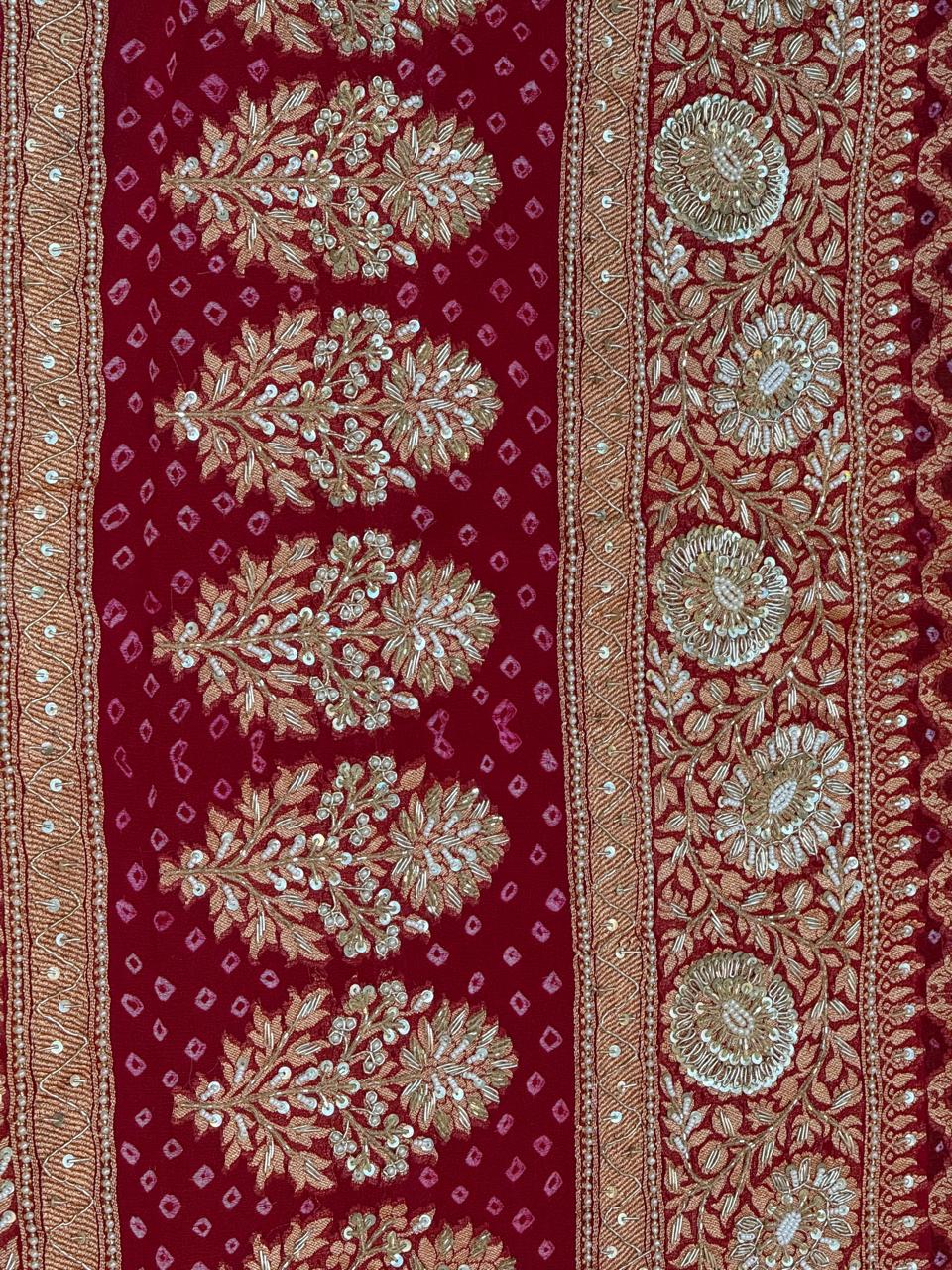 Close-up detail of heavy gold zardozi and sequin hand-embroidery forming repetitive floral trees, vines, and circular medallions on a crimson red bandhani dupatta border.