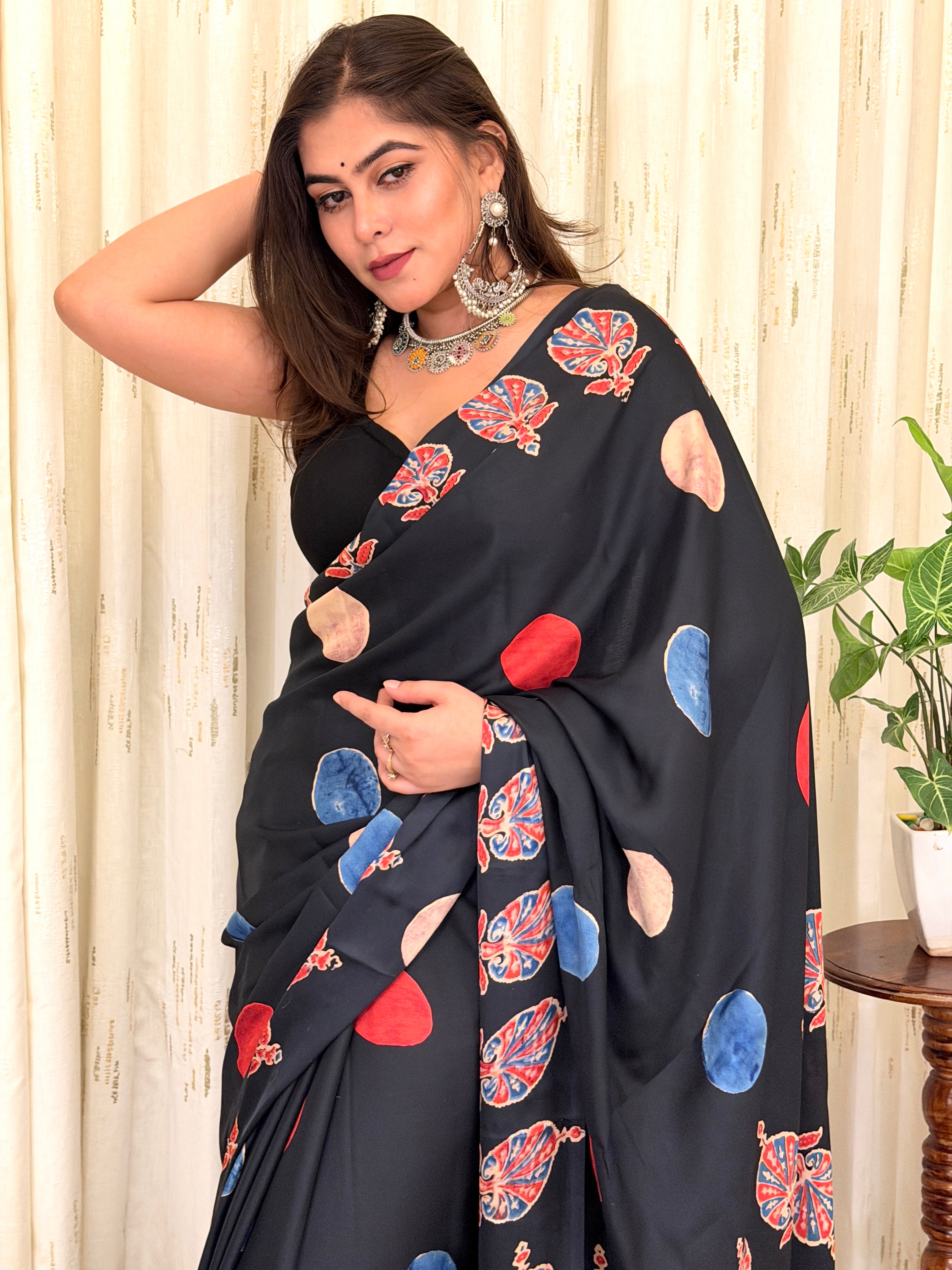 Close-up mid-shot of the black crepe designer saree showcasing the drape, colorful abstract circular prints, and detailed ethnic borders.