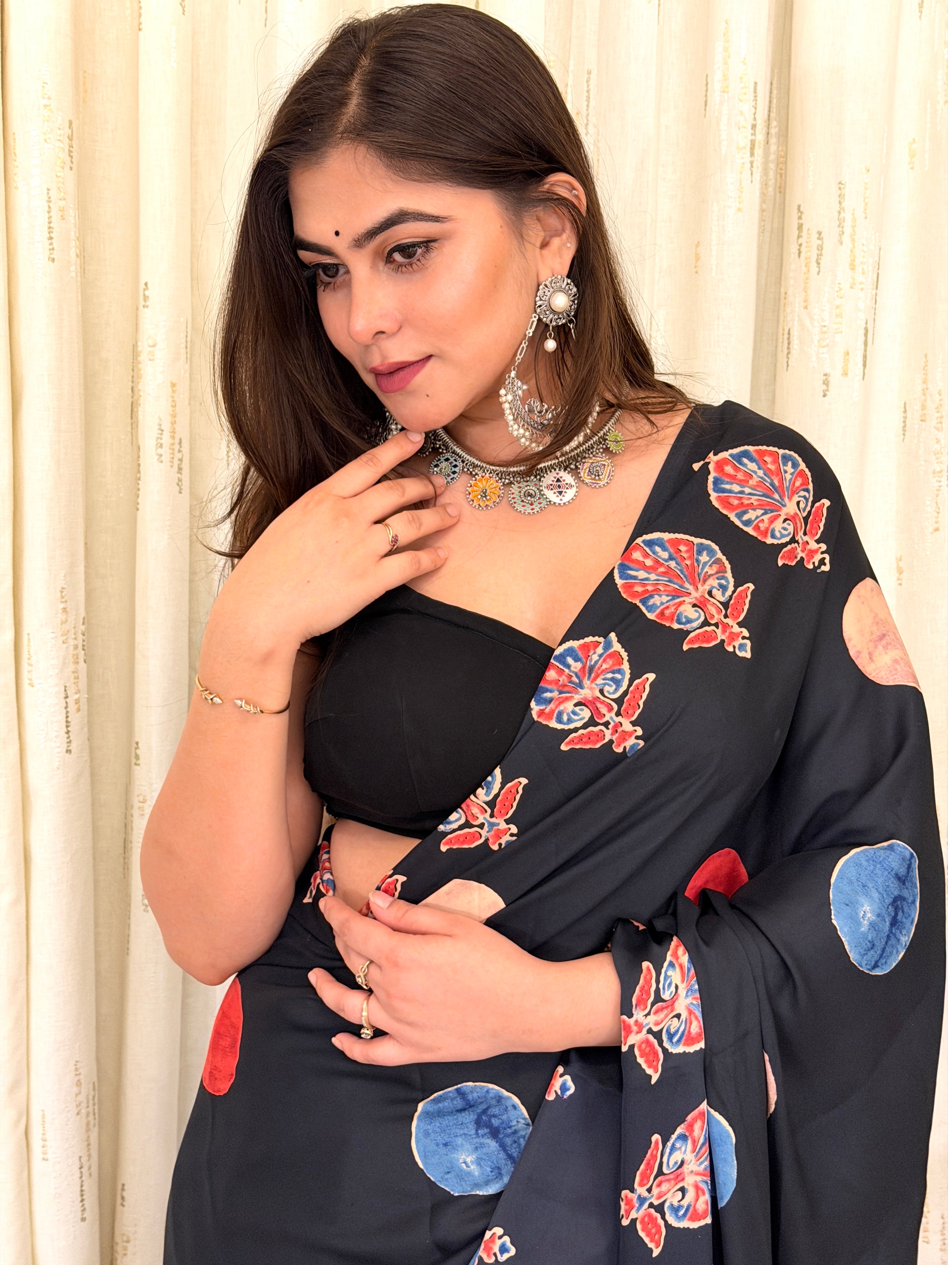 Detailed close-up of the black crepe saree's pallu showing the red and blue leaf-like Kalamkari patterns paired with statement silver oxidized jewelry.