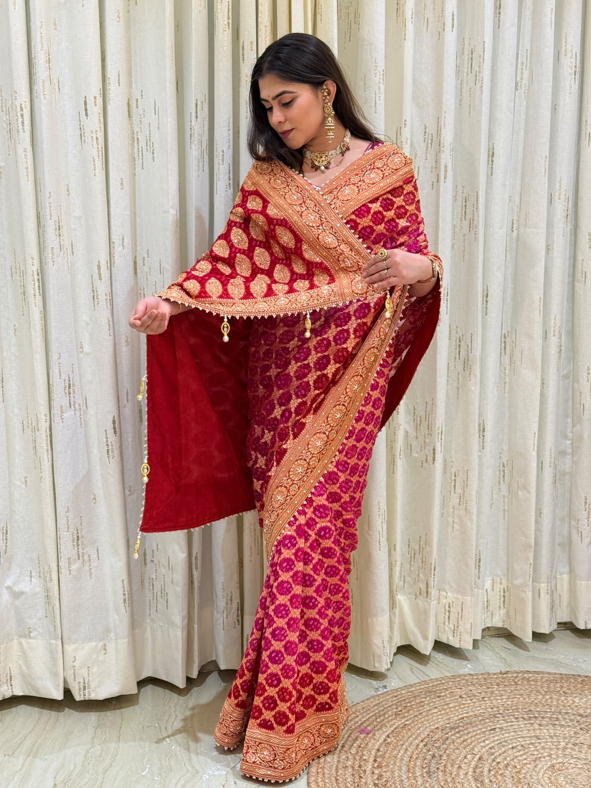 "Vibrant rani pink and deep red Bandhani print saree featuring heavy gold zari embroidery, scalloped borders, and pearl tassels."