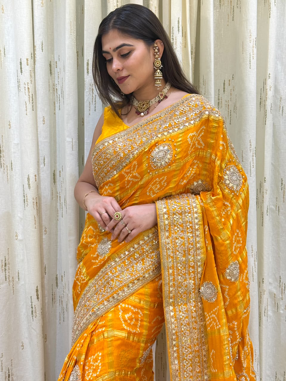 "Vibrant mango yellow Bandhani saree featuring heavy gold zari embroidery, mirror-work borders, and circular medallion motifs."