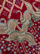 Close-up of a rich red bridal dupatta showcasing heavy gold zari and white pearl hand-embroidery. The intricate design features traditional motifs including majestic cranes, a decorated elephant, and floral vines over a textured red background with subtle dot patterns.