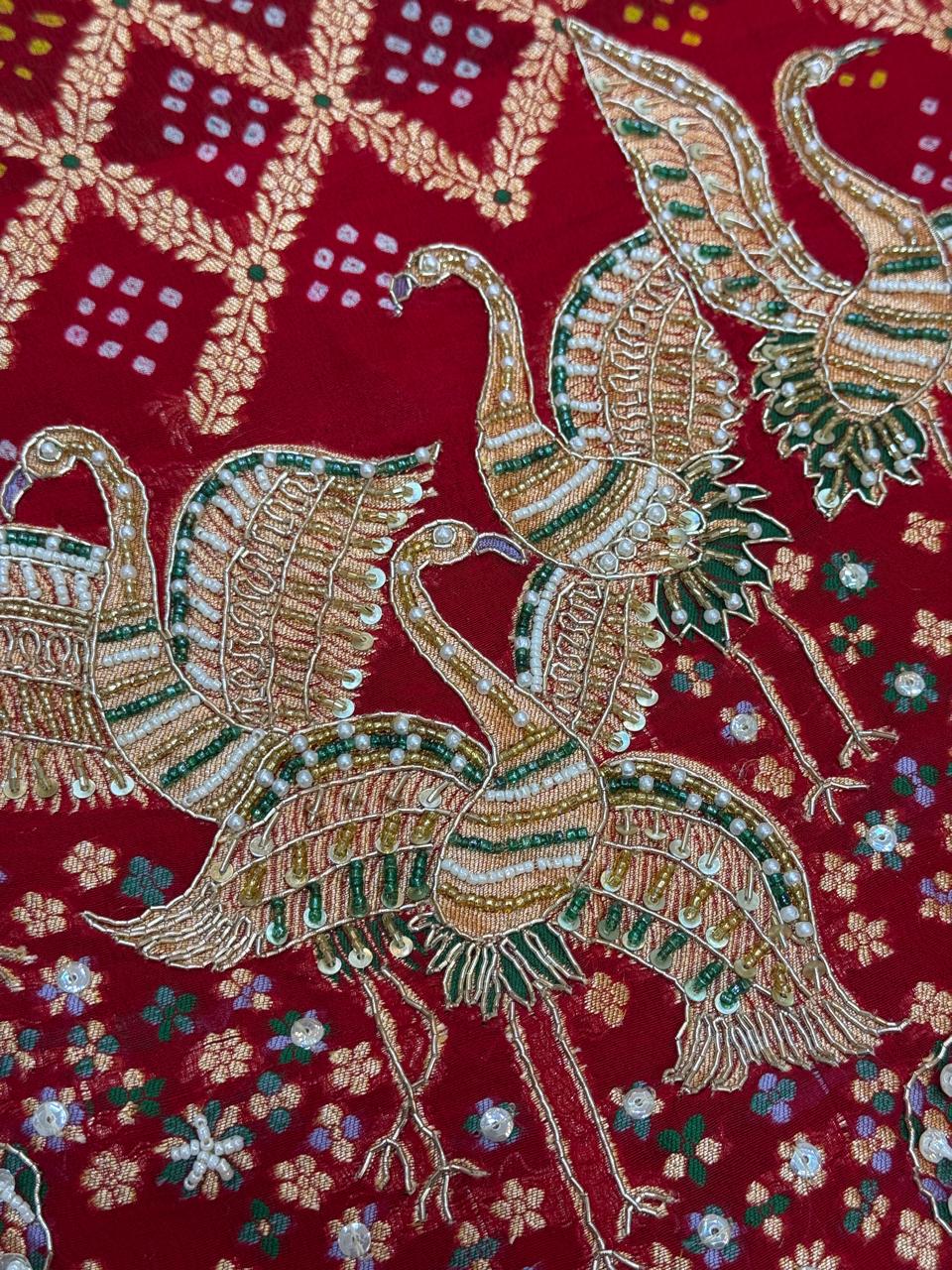 Close-up of a rich red bridal dupatta showcasing heavy gold zari and white pearl hand-embroidery. The intricate design features traditional motifs including majestic cranes, a decorated elephant, and floral vines over a textured red background with subtle dot patterns.
