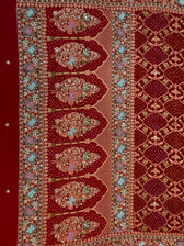 Close-up detail of a crimson red dupatta showing intricate gold zardozi, sequin, and pastel thread hand-embroidery forming large floral bouquets inside traditional architectural arches over a bandhani print.
