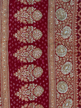 Close-up detail of heavy gold zardozi and sequin hand-embroidery forming repetitive floral trees, vines, and circular medallions on a crimson red bandhani dupatta border.